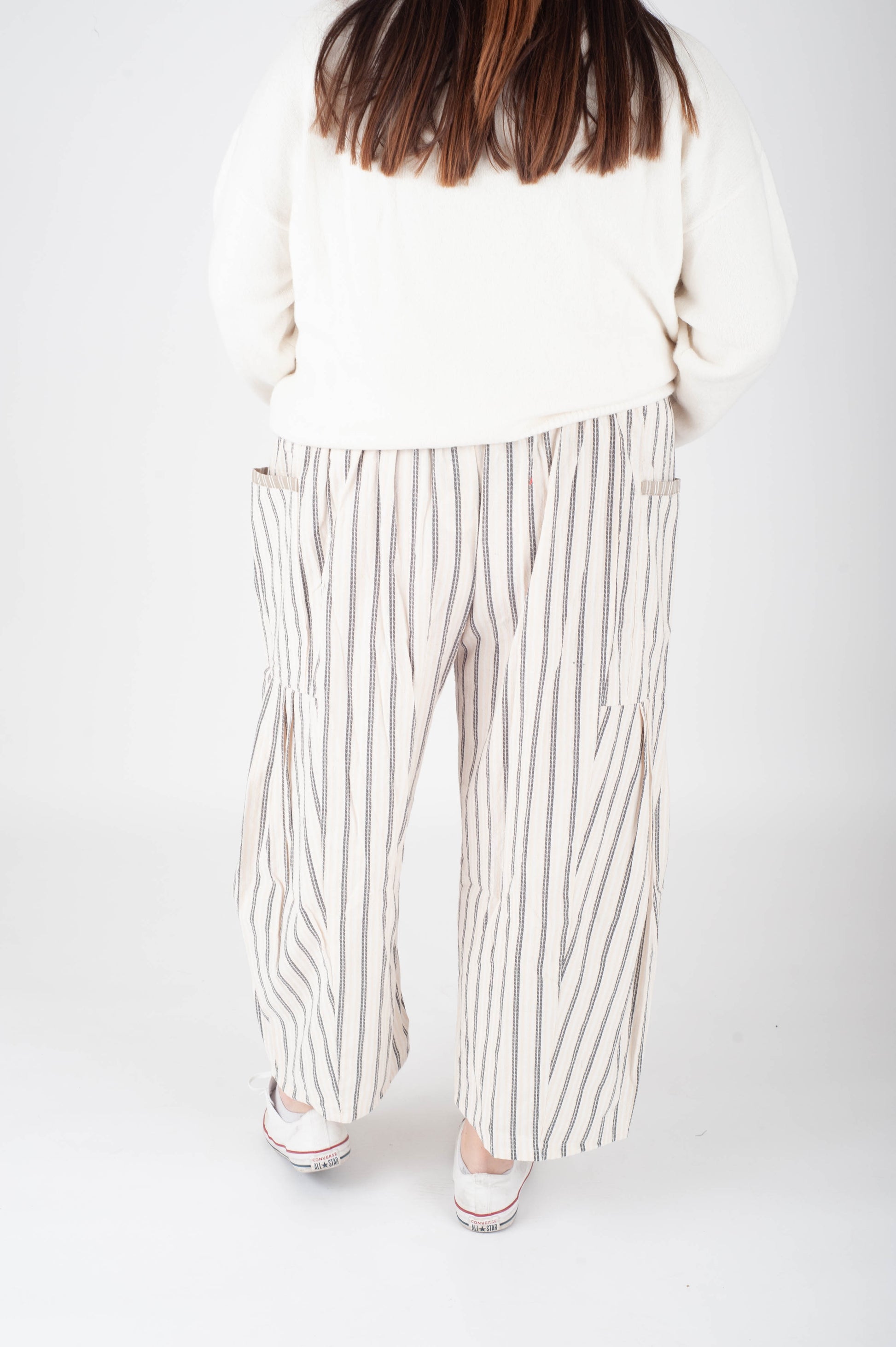 Person wearing a white sweater and striped pants on a plain background