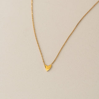 Gold heart-shaped pendant necklace on a beige background