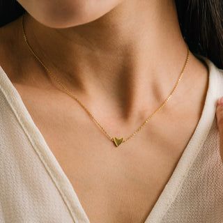 Gold necklace with a heart pendant worn by a person in a neutral setting
