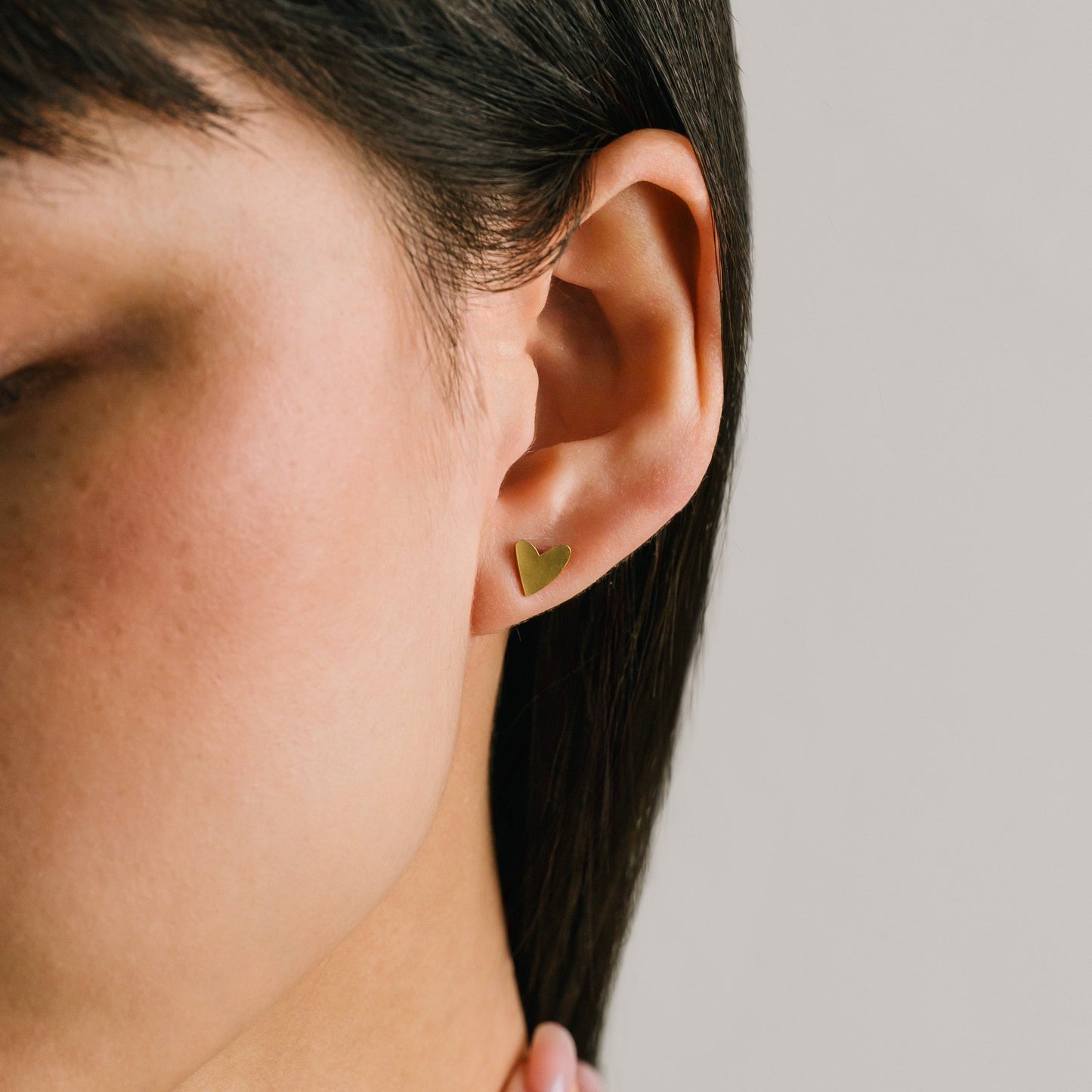 Heart-shaped gold earring worn by a person on a neutral background