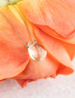Clear teardrop pendant necklace on a pink rose