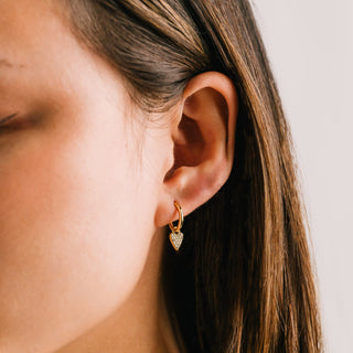 Close-up of a person wearing a gold earring with a clear gemstone.