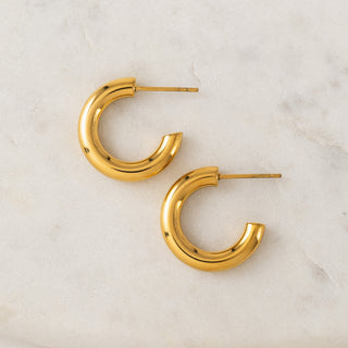 A pair of gold-colored hoop earrings on a marble surface