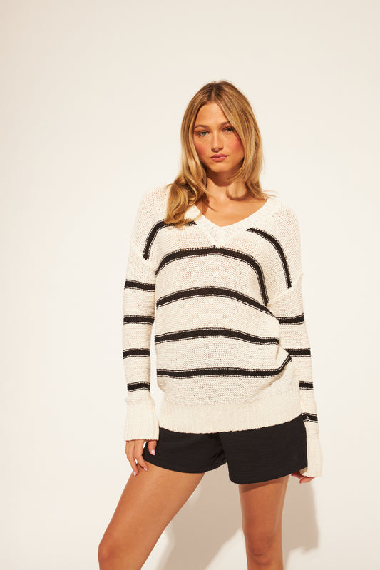 Woman wearing a white sweater with black stripes and black shorts on a plain background