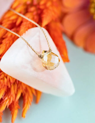 Gold necklace with a pendant on a white triangle against an orange and blue background