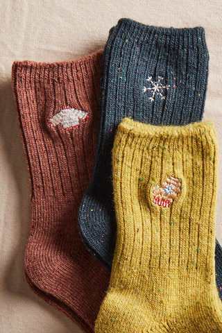 Three pairs of knitted socks in brown, blue, and yellow with embroidered designs on a beige background.