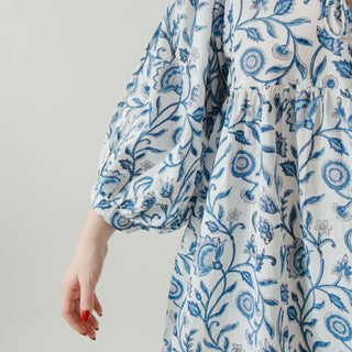 White dress with blue floral pattern worn by a person on a plain background