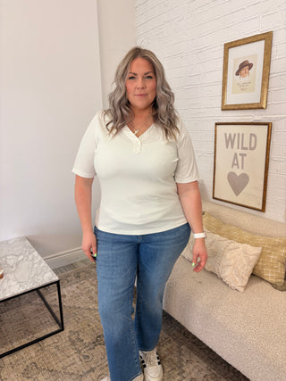 Woman standing in a living room wearing a white top and blue jeans.
