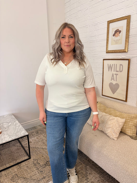 Woman standing in a living room wearing a white top and blue jeans.