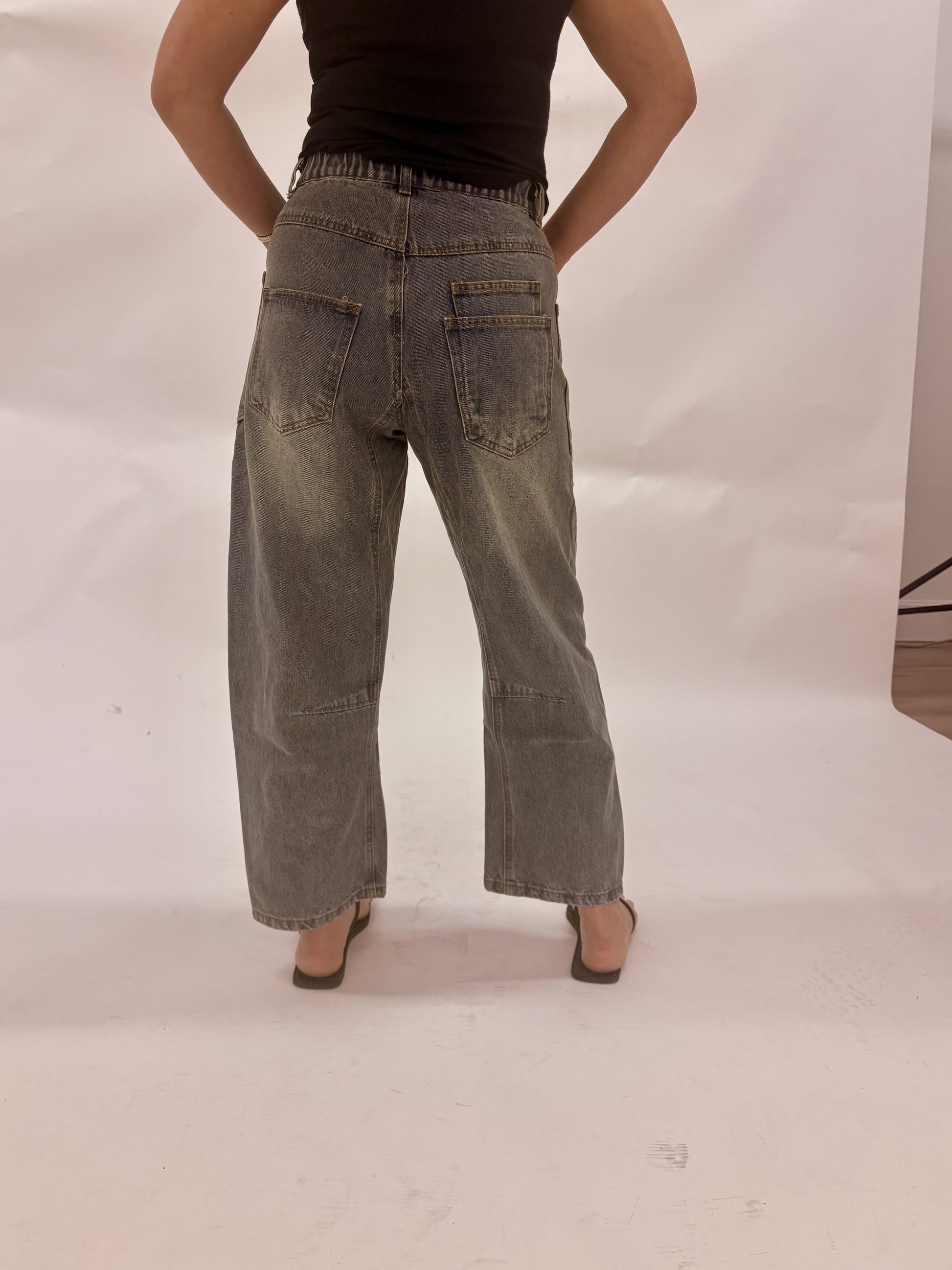 Person wearing wide-leg jeans and a black top on a plain background
