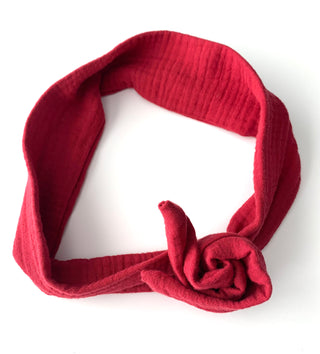 A red textured cotton muslin headband with a knotted bow detail, displayed on a clean white background.