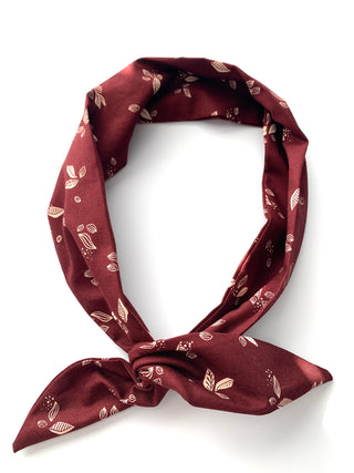 A burgundy silk scarf with a delicate beige leaf and floral pattern, tied in a knot on a clean white background.