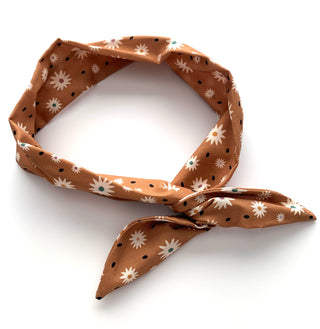 A brown silk scarf with a white daisy and black polka dot pattern, tied in a knot on a white background.