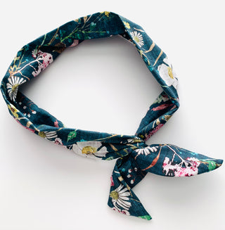 A dark teal fabric headband with a colorful floral and daisy pattern, tied in a knot at the bottom right, displayed on a clean white background.