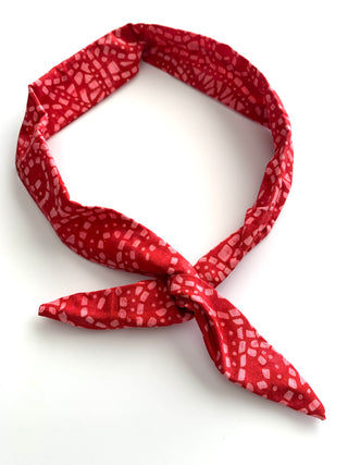 A red fabric headband with a white abstract geometric pattern, tied in a knot at the front, displayed on a clean white background.