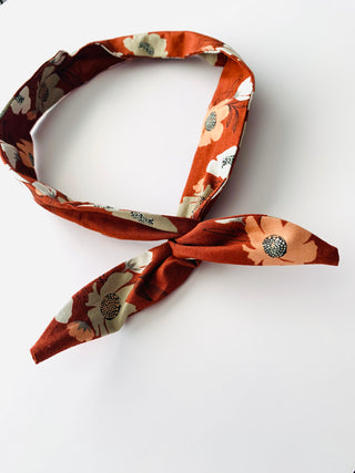 A floral necktie scarf in rust orange, peach, and cream, tied in a knot and displayed on a clean white background.