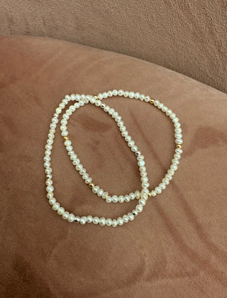 A double-strand pearl necklace with small gold spacer beads, resting on a brown textured fabric surface.