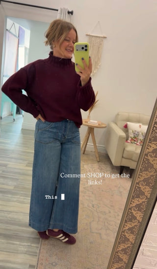 Women taking a selfie in the mirror wearing a burgundy sweater and jeans. 