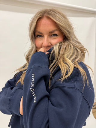 Woman wearing a navy blue hoodie with 'Stitch & Stone' logo, posing against a white background