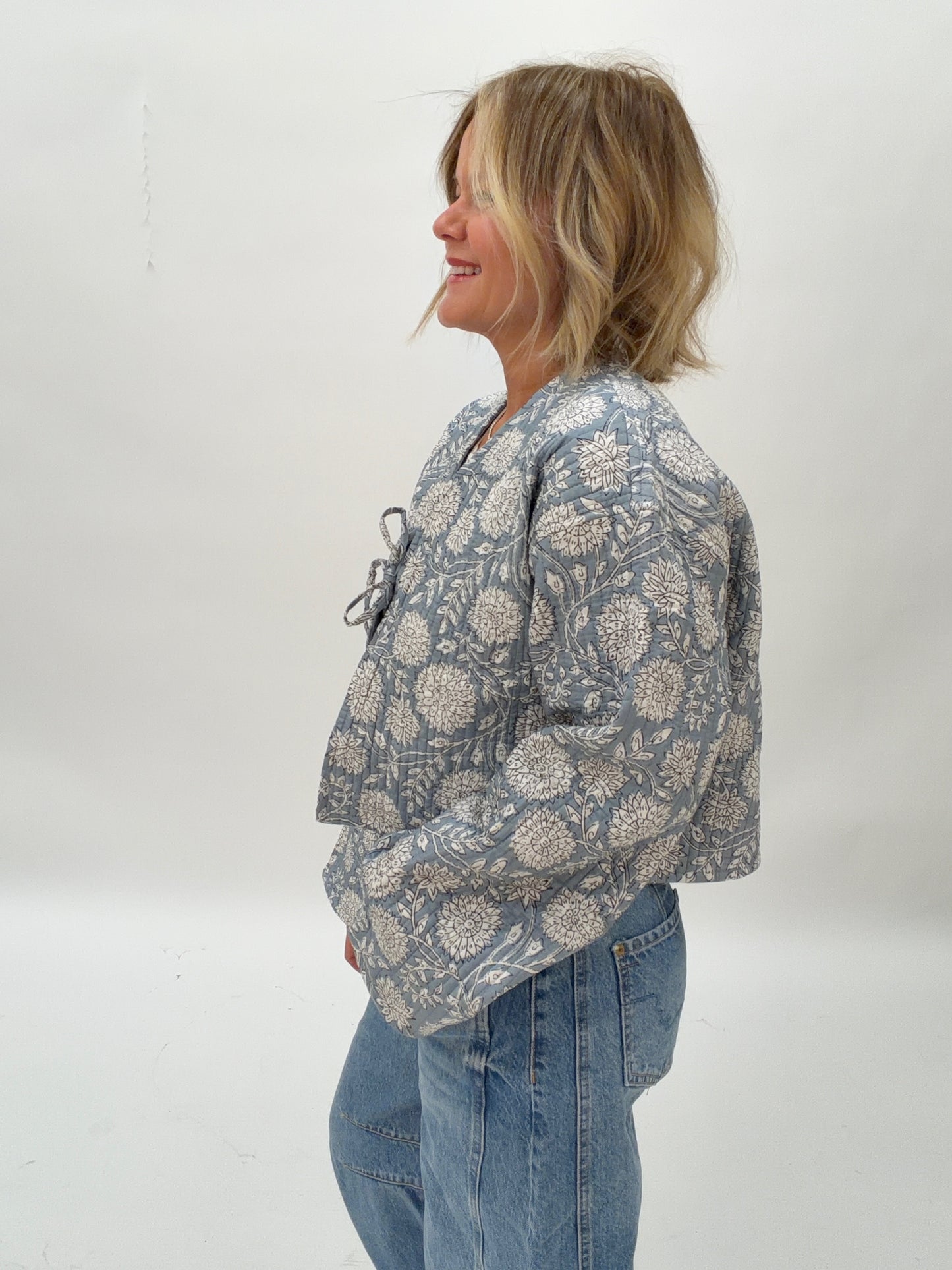 Person wearing a patterned jacket and jeans against a white background