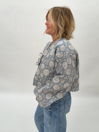 Person wearing a patterned jacket and jeans against a white background