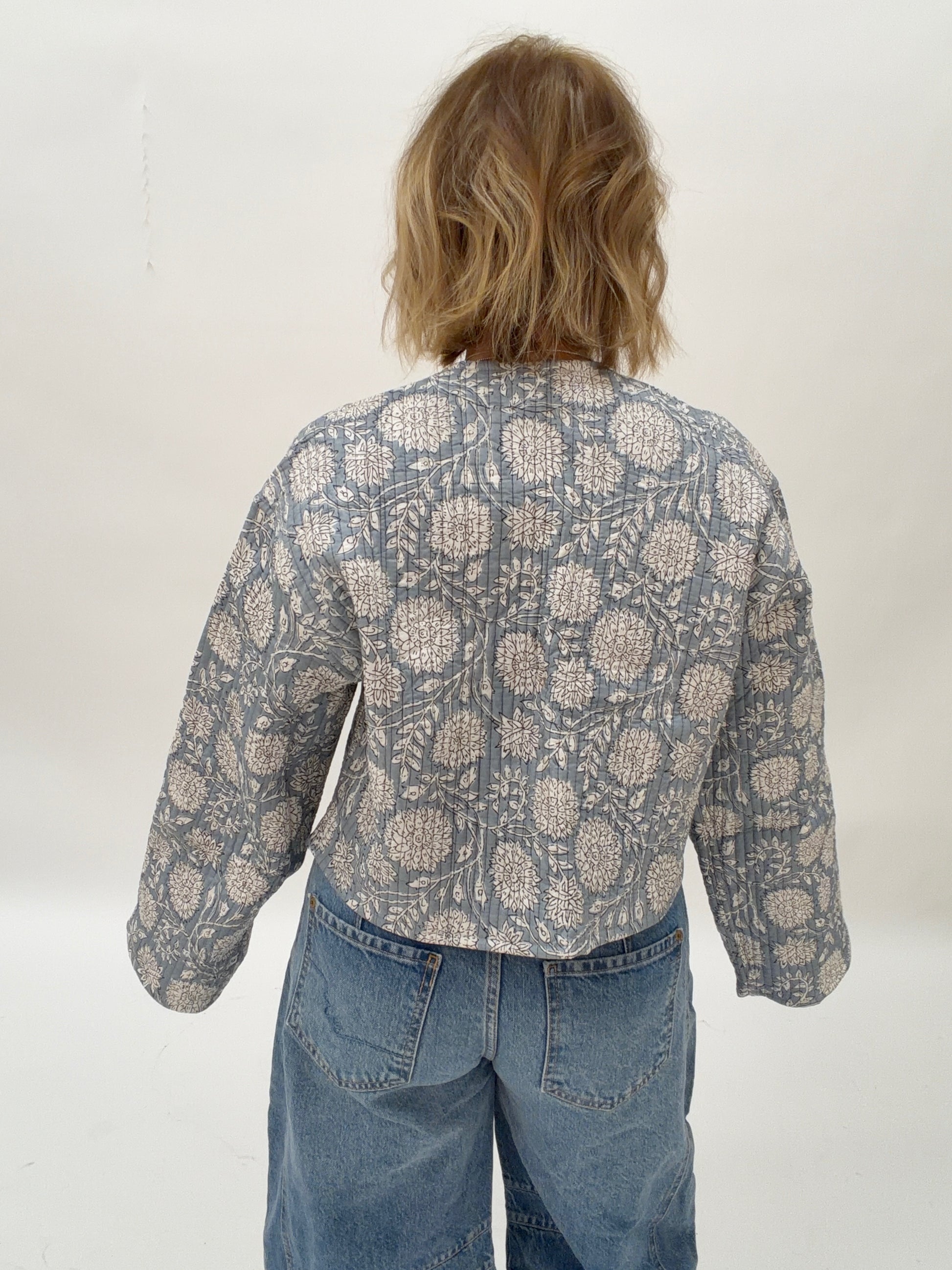 Person wearing a patterned shirt and jeans against a white background