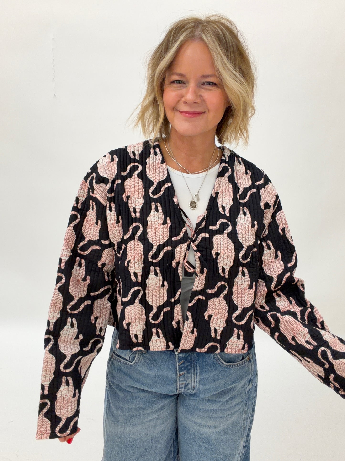 Woman wearing a black cardigan with pink cat pattern and blue jeans on a white background