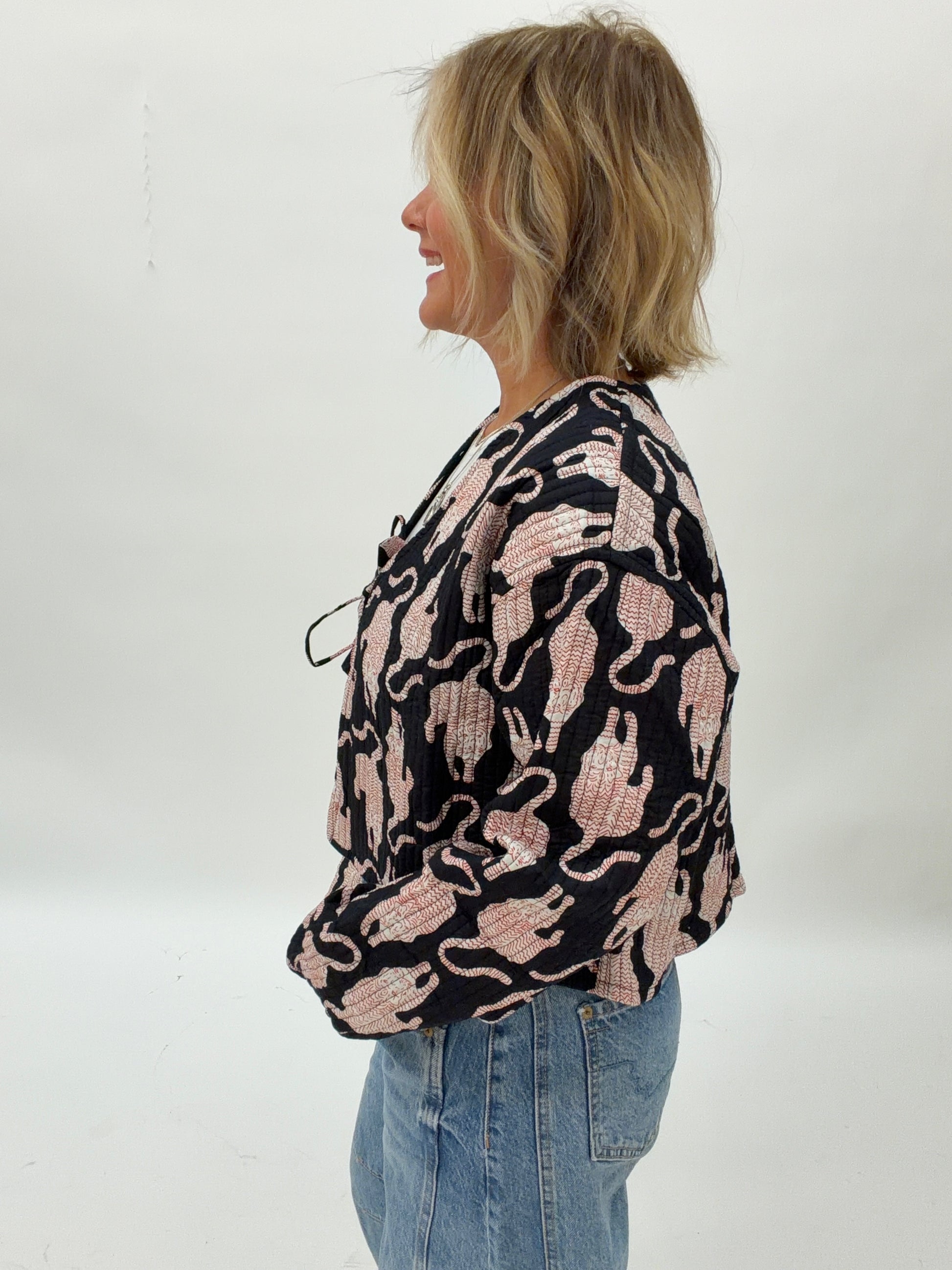 Woman wearing a black blouse with pink cat pattern and blue jeans on a white background