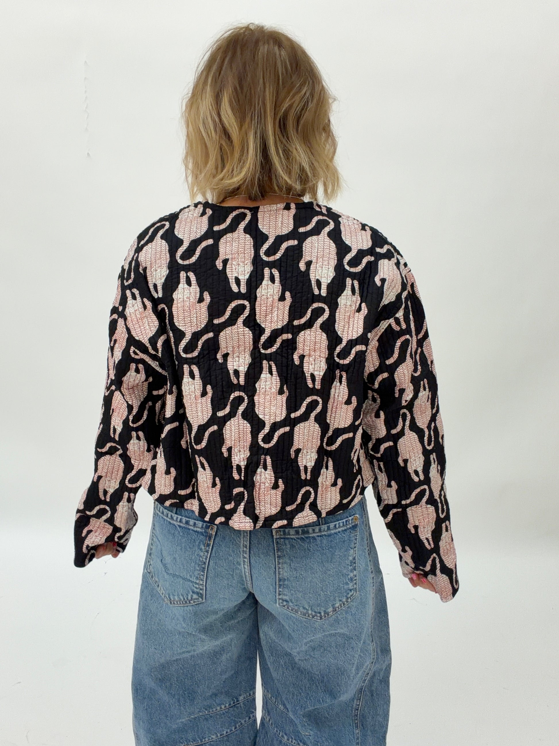 Person wearing a black long-sleeve shirt with pink cat pattern and blue jeans on a white background