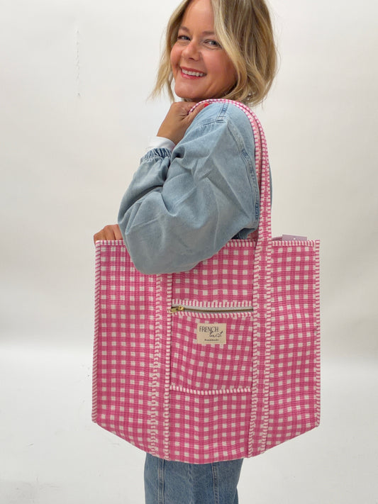 Person holding a pink gingham tote bag with a visible brand label against a white background