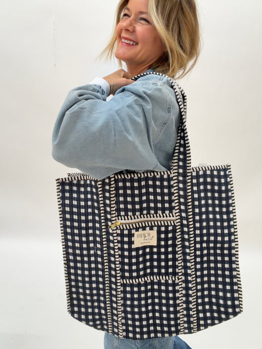 Person holding a black and white checkered bag with a visible brand label on a plain background