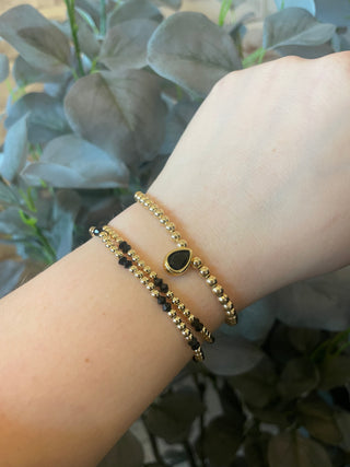 Gold bracelets on a wrist with a blurred plant background