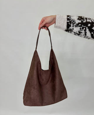 Brown handbag held by a person wearing a patterned sweater on a light gray background