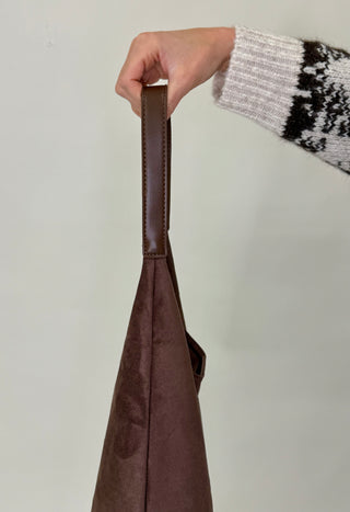 Brown bag held by a hand with a patterned sleeve against a plain background