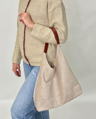 Person wearing a beige sweater and holding a matching beige tote bag against a plain background