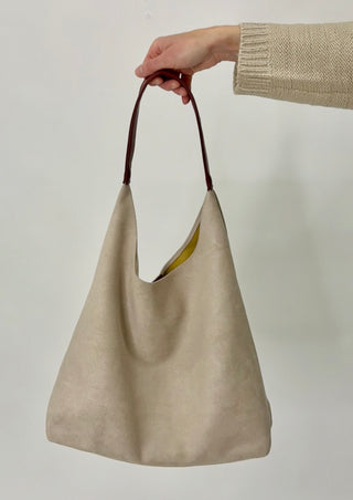 Beige handbag with brown handle held by a person against a plain background