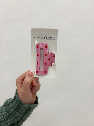 A hand holding a pink and white patterned hair clip against a white background, with the brand 'Stitch & Stone' visible on the packaging.
