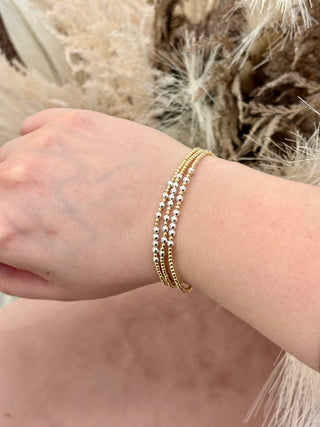 A gold-colored bracelet with small beads, worn on a person's wrist.