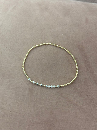 A gold-colored bracelet with small beads, worn on a person's wrist.