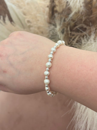 A bracelet featuring white pearls and silver beads displayed on a person's wrist.