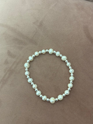 A bracelet featuring white pearls and silver beads displayed on a person's wrist.