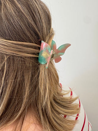 A person with a butterfly-shaped hair clip in multicolor tones attached to their hair.