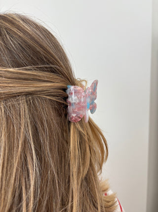 A person with a butterfly-shaped hair clip in multicolor tones attached to their hair.
