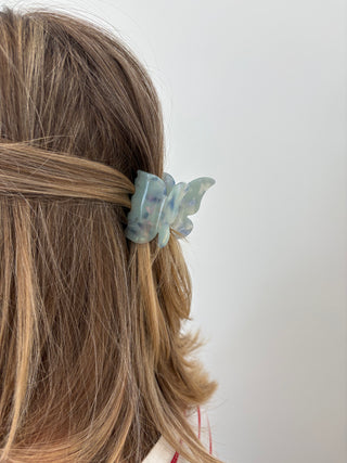 A person with a butterfly-shaped hair clip in multicolor tones attached to their hair.