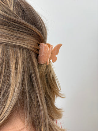 A person with a butterfly-shaped hair clip in multicolor tones attached to their hair.