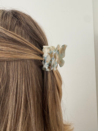 A person with a butterfly-shaped hair clip in multicolor tones attached to their hair.