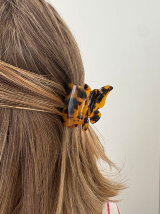 A person with a butterfly-shaped hair clip in multicolor tones attached to their hair.