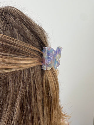 A person with a butterfly-shaped hair clip in multicolor tones attached to their hair.
