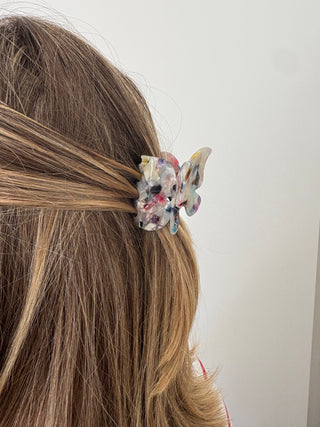 A person with a butterfly-shaped hair clip in multicolor tones attached to their hair.