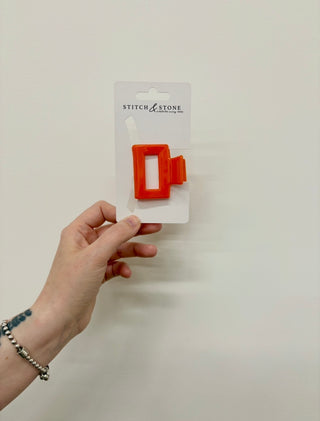 Red hair clip on a 'Stitch & Stone' branded card held by a hand against a white background